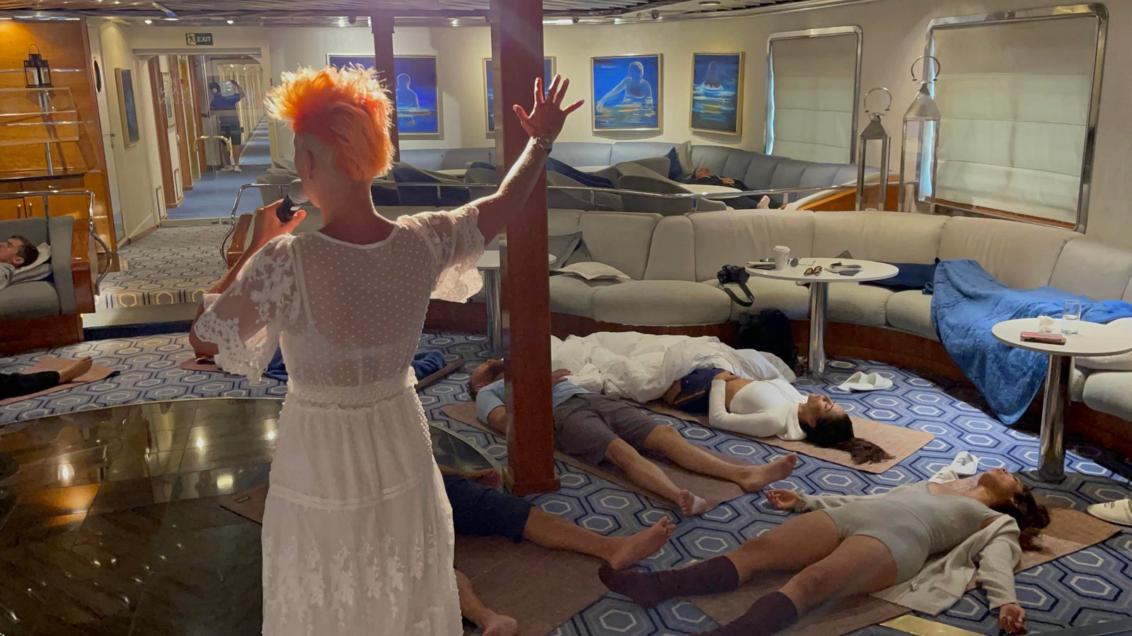 Facilitator with a microphone guiding participants who lie on mats and sofas during a breathwork session in a lounge setting