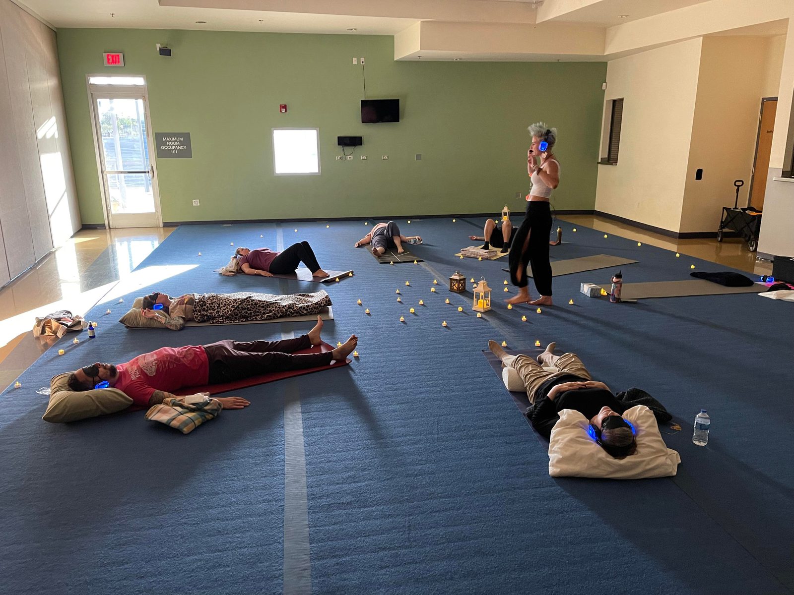 Participants lying on mats wearing headphones and eye masks during a supervised breathwork session while a facilitator guides from the centre of the room